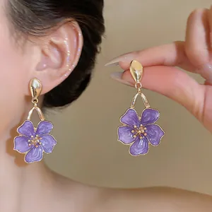 Detail view of sweet style purple enamel flower drop earrings shown on ear and hand