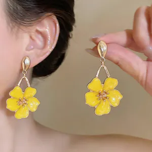 Close-up of vibrant yellow flower drop earrings with golden accents on a model