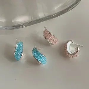 Dettaglio di orecchini a cerchio ritorti in argento con cristalli blu e rosa.
