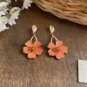 Close-up of sweet style orange flower enamel pendant earrings on wooden background.