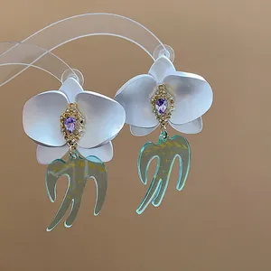 Vue détaillée de boucles d'oreilles fleur d'orchidée en résine avec strass violets et hirondelles.