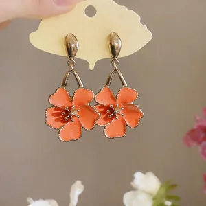 Close-up of sweet orange oil-drop flower earrings on a cloud-shaped display card.