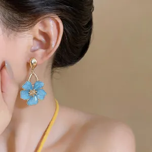 Close-up of sweet blue enamel flower drop earrings worn by a model in soft light.