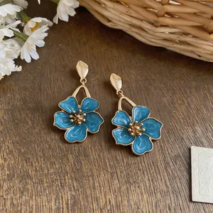 Detailed view of blue enamel flower drop earrings on a rustic wooden background