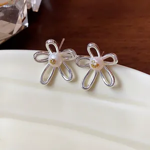 Close-up of silver hollow flower stud earrings with elegant pearls and gold accents