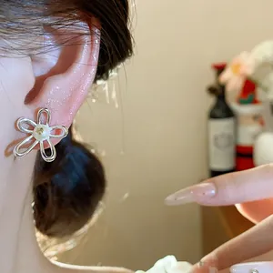 Close-up detail of hollow silver-tone flower stud earring with a pearl center.
