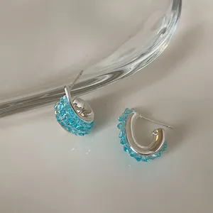 Dettaglio di orecchini a cerchio intrecciati con cristalli blu