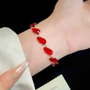 Detail shot of a luxurious red teardrop zircon bracelet on a woman's wrist with gold plating.
