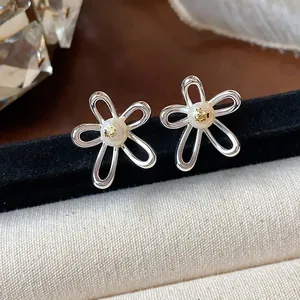 Close-up macro detail of silver hollow flower stud earrings with a central pearl inlay