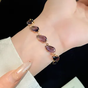 Detailed view of a delicate gold-tone bracelet featuring sparkling teardrop purple zircons