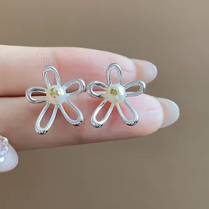 Detail view of silver-toned hollow flower stud earrings with pearl centers on a finger