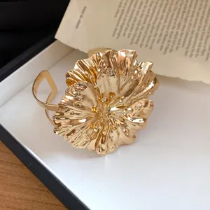 Close-up of gold pleated flower detail on a metallic double-layer cuff bracelet