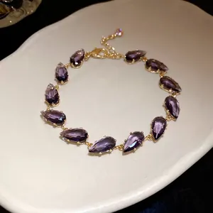 Detailed macro view of an elegant purple teardrop zircon bracelet on white ceramic.