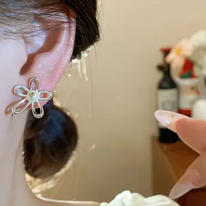 Detail view of a hollow silver flower earring with a pearl center on a model