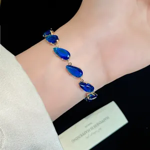 Close-up of elegant gold bracelet with sparkling blue teardrop zircon stones on wrist.