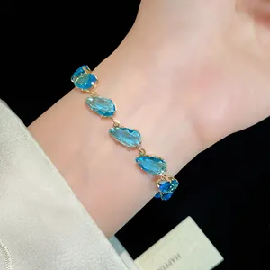 Detail view of a luxury gold bracelet with sparkling blue teardrop zircons on a wrist.
