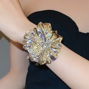 Detailed shot of a large gold metallic flower cuff bracelet worn on a female wrist.