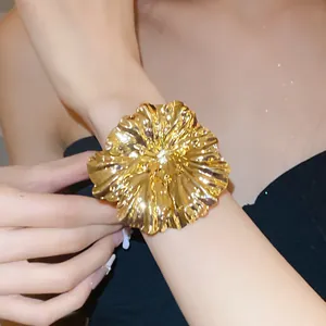 Detailed view of a large metallic golden pleated flower open bangle on a woman's wrist