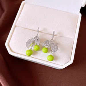 Close-up of sparkling silver cherry earrings with vibrant green fruit and zirconia leaves.