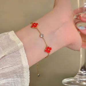 Detalle de una delicada pulsera de oro con colgantes de flores rojas y circón claro