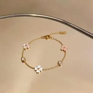 Primer plano detallado de una pulsera de acero inoxidable dorada con flores y circonitas