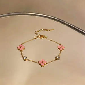 Elegante pulsera de acero dorado con flores rosas y circonitas claras, vista de detalle.