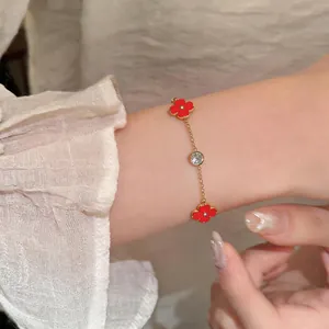 Primer plano de una pulsera dorada con flores rojas y circonitas brillantes en la muñeca.