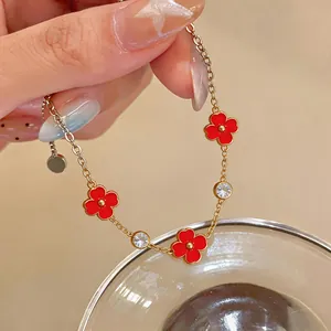 Detalle de una pulsera dorada de acero inoxidable con flores rojas y cristales brillantes.