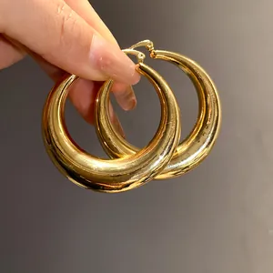 Close-up detail of chunky gold-toned hoop earrings with a high-polish metallic shine