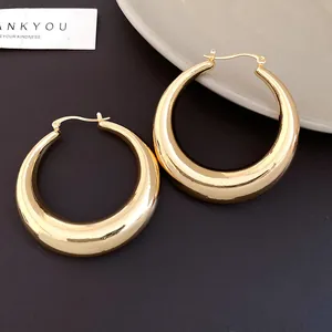 Detailed view of shiny gold-toned chunky tapered hoop earrings on dark background
