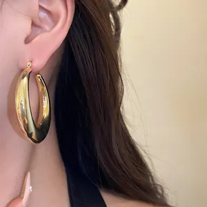 Close-up view of elegant high-shine gold chunky hoop earrings worn by a model for fashion