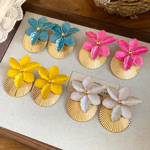 Macro view of colorful enamel flower earrings with pleated gold texture on wooden tray