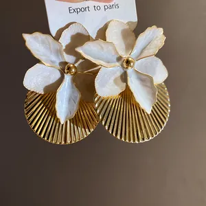 Macro view of elegant white enamel flower earrings featuring intricate gold pleated texture.