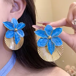 Close-up of vibrant blue enamel flower earrings with pleated gold texture detail