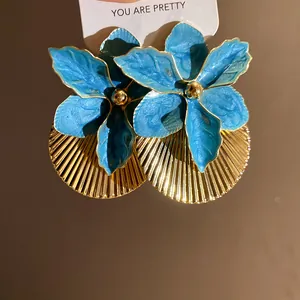 Macro view of blue enamel flower earrings featuring detailed pleated gold texture