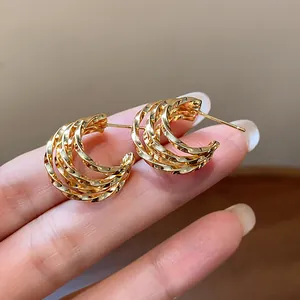 Detail shot of 18k gold plated multi-layered C-shaped stud earrings held in hand