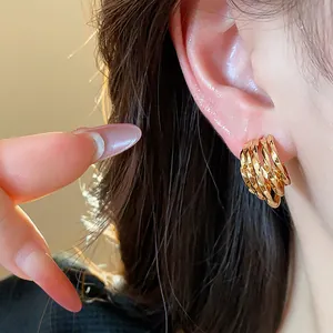 Close-up of 18k gold plated multi-layer C-shaped stud earrings worn on ear.