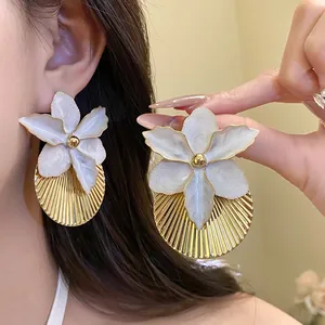 Detailed close-up of white enamel flower earrings with golden pleated texture