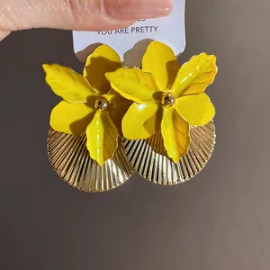 Detail of yellow enamel flower earrings with gold pleated texture on a white card.