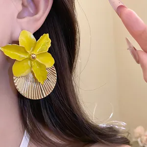 Close-up detail of yellow enamel flower earrings with a gold textured round disc