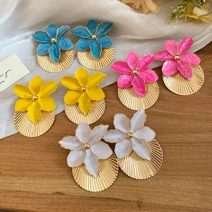 Detail of colorful enamel flower earrings with gold pleated texture on wooden surface.