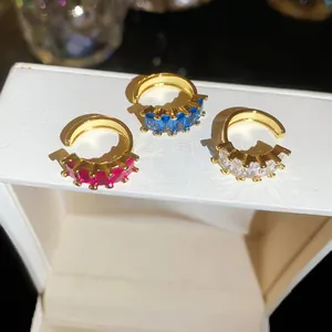 Detail of three 18k gold-plated square zircon ear cuffs in red, blue, and white colors