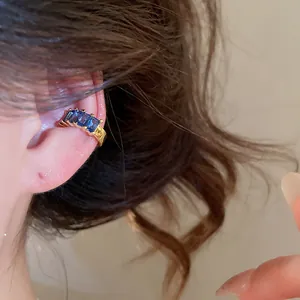 Macro view of a blue zircon 18k gold plated square ear cuff worn on a model's ear