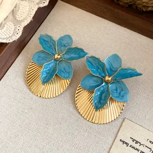 Detail shot of blue enamel flower earrings with pleated gold discs on linen.