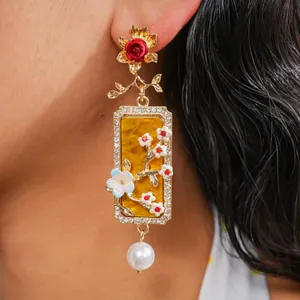 Détail de boucles d'oreilles de style palais avec fleurs en résine et perles pendantes.