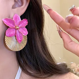 Macro detail of pink enameled flower earring with golden pleated texture worn by model
