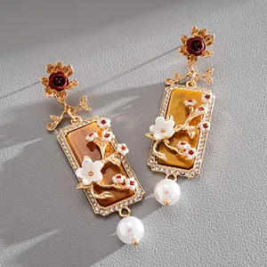 Vue détaillée de boucles d'oreilles dorées style palais avec fleur en résine et perle