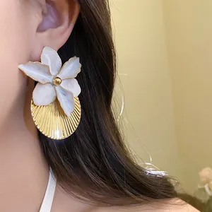 Close-up view of white enamel flower earrings with gold pleated texture on model's ear