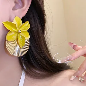 Close-up detail of a yellow floral orchid earring with a golden pleated texture base