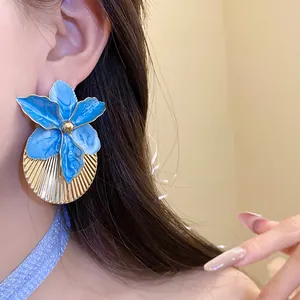 Close-up of elegant blue oil-drop flower earrings with gold pleated texture on a model.